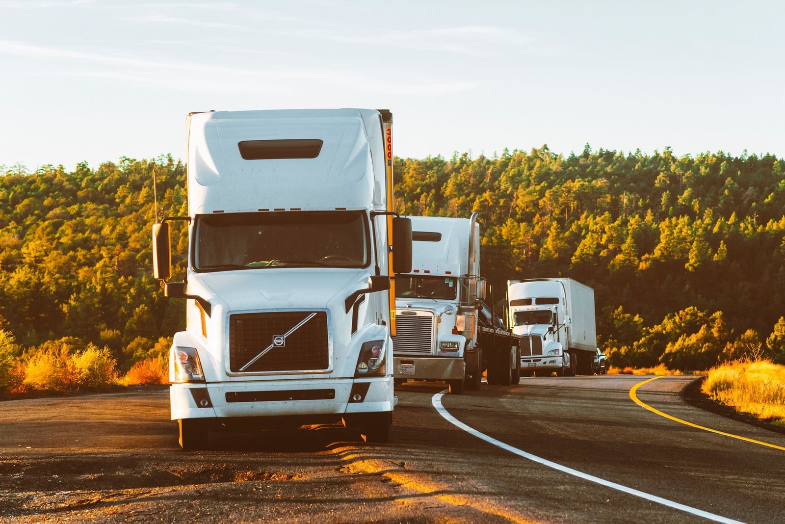 Three semi-trucks driving along a highway at golden hour