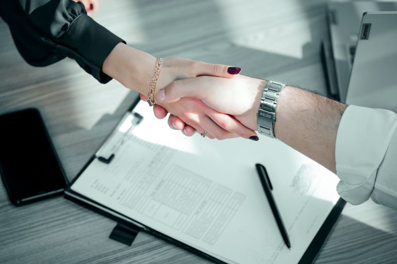Two people shaking hands over a signed rate agreement on a desk